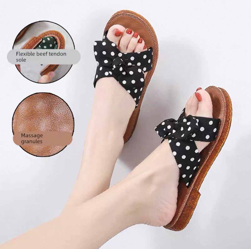 Black polka dot sandals with bows worn by a person on a light gray background