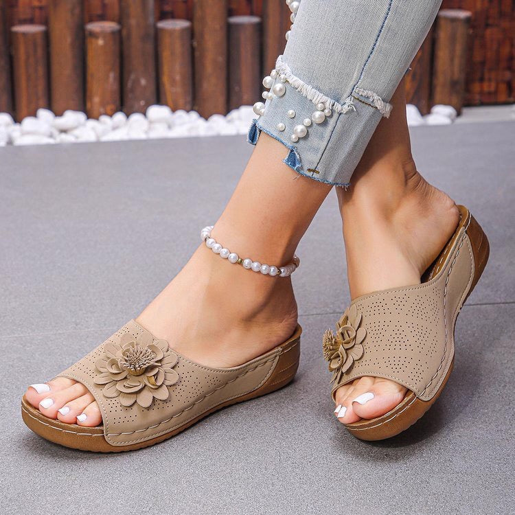 Beige sandals with floral designs worn by a person on a gray surface.