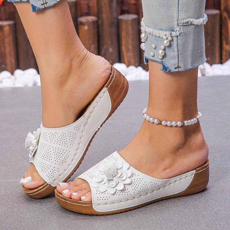 White sandals with brown soles worn by a person, with a blurred background.