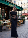 Woman in a black off-shoulder dress standing on a street with a café in the background