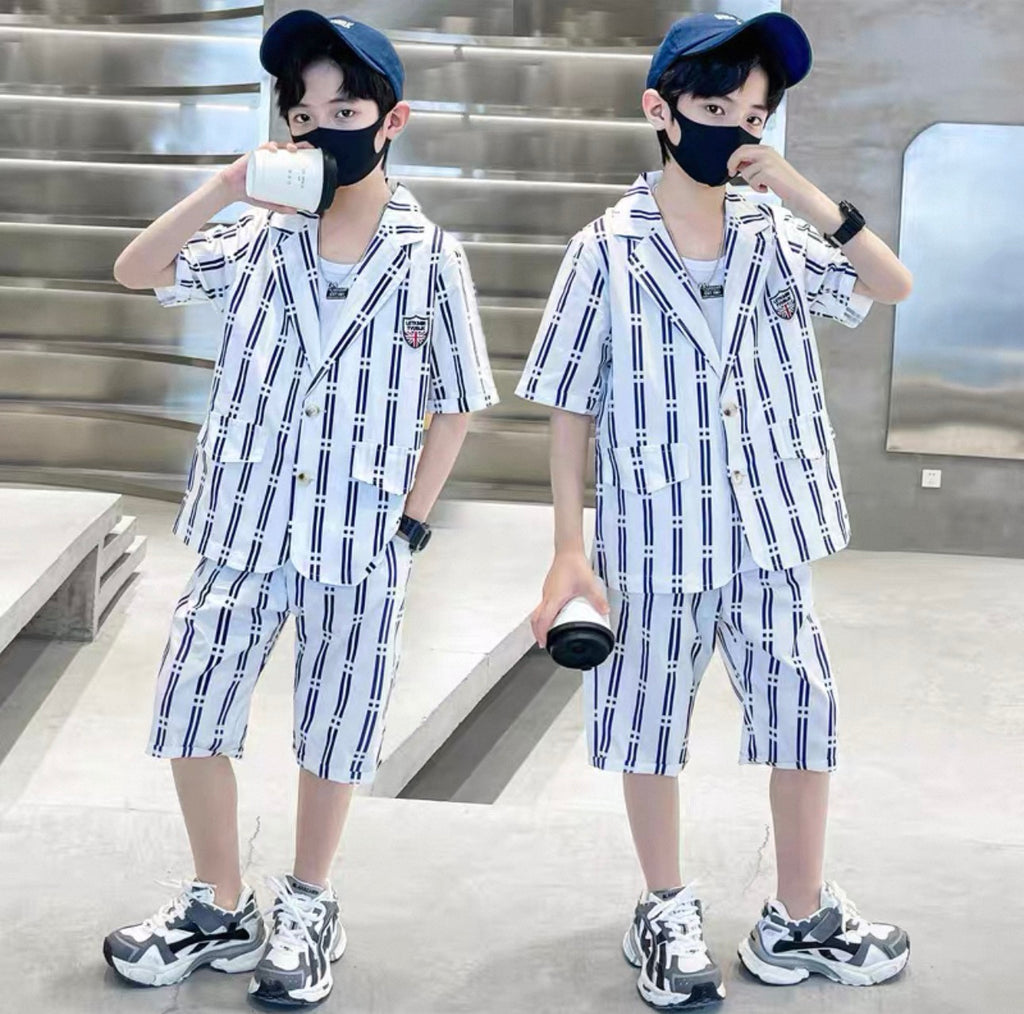Two children wearing matching outfits with plaid shirts and shorts, standing indoors.