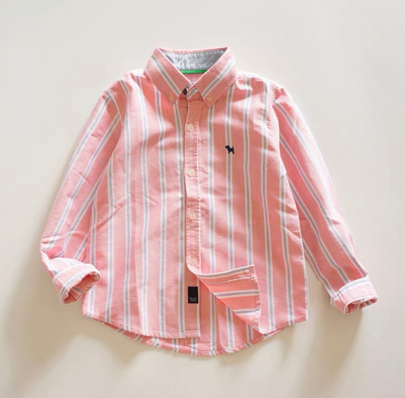 Pink and white striped shirt with a small logo on a light background