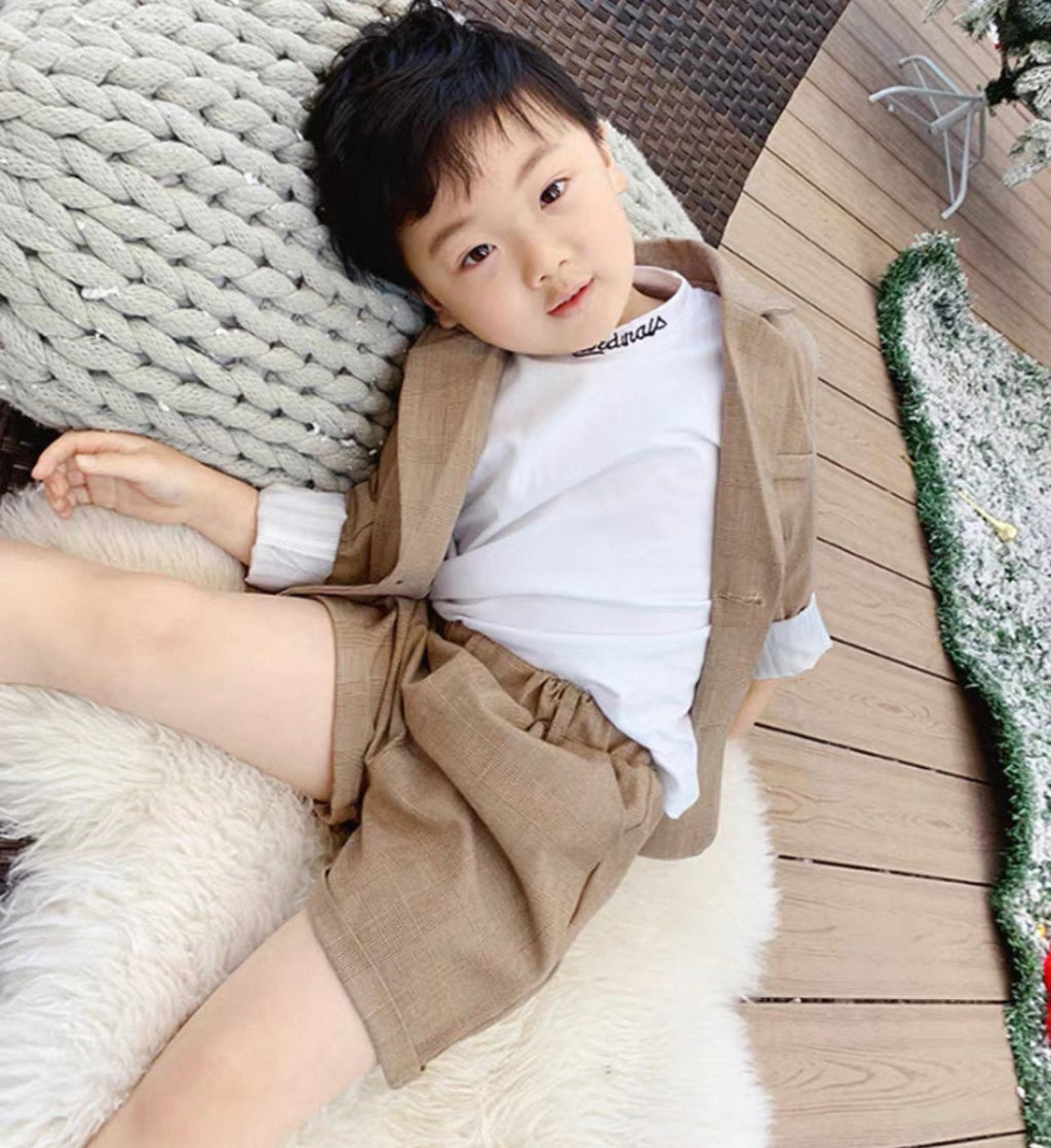 Child wearing a beige outfit with suspenders lying on a textured surface