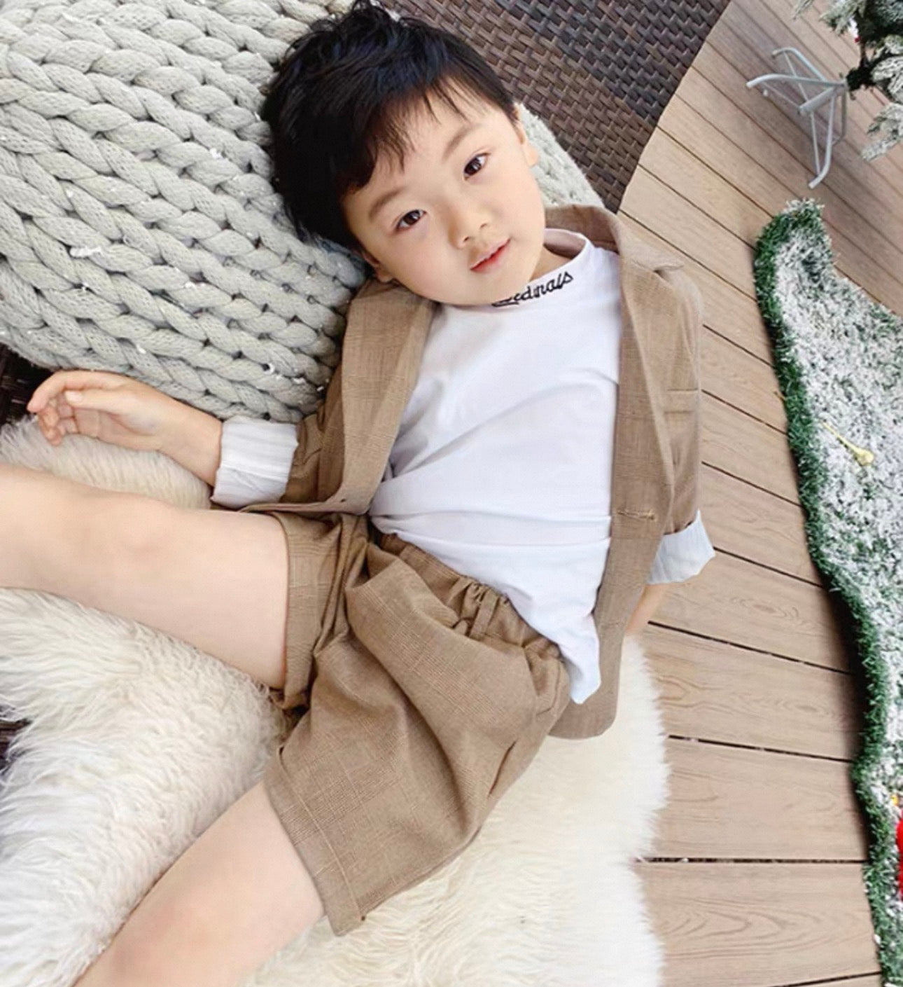 Child wearing a beige outfit with suspenders lying on a textured surface