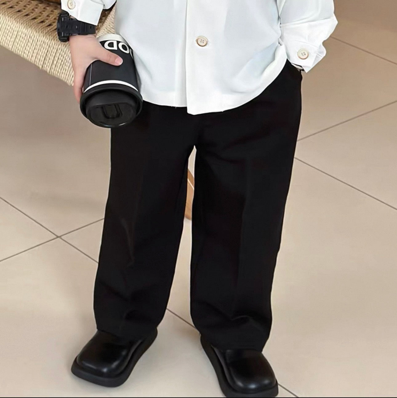 Person wearing a white shirt and black pants holding a black container with a brand logo.