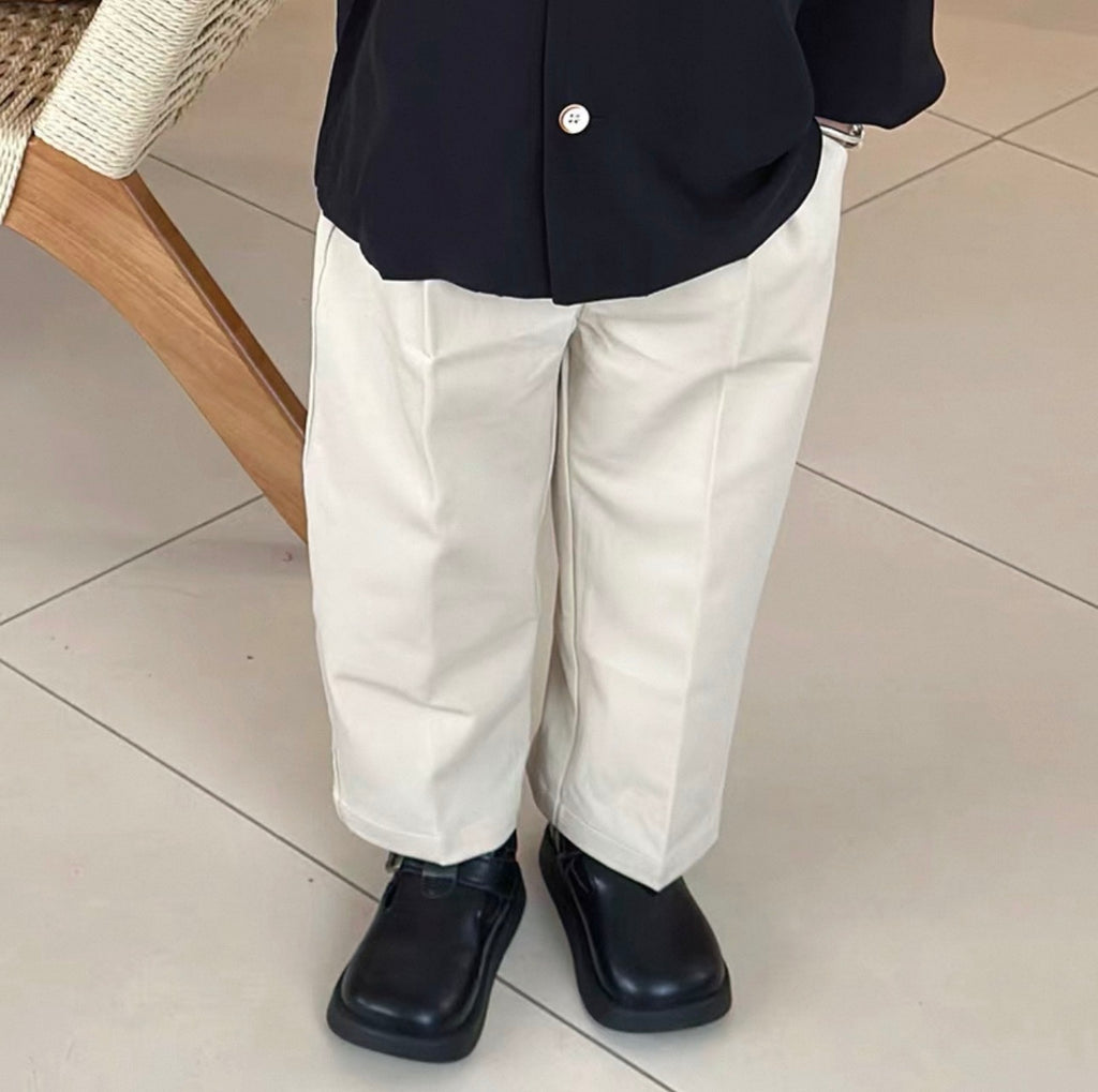 Person wearing a navy blazer, white pants, and black shoes on a tiled floor.