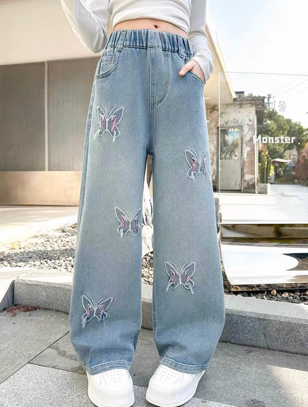 Light blue jeans with butterfly embroidery worn by a person outdoors.