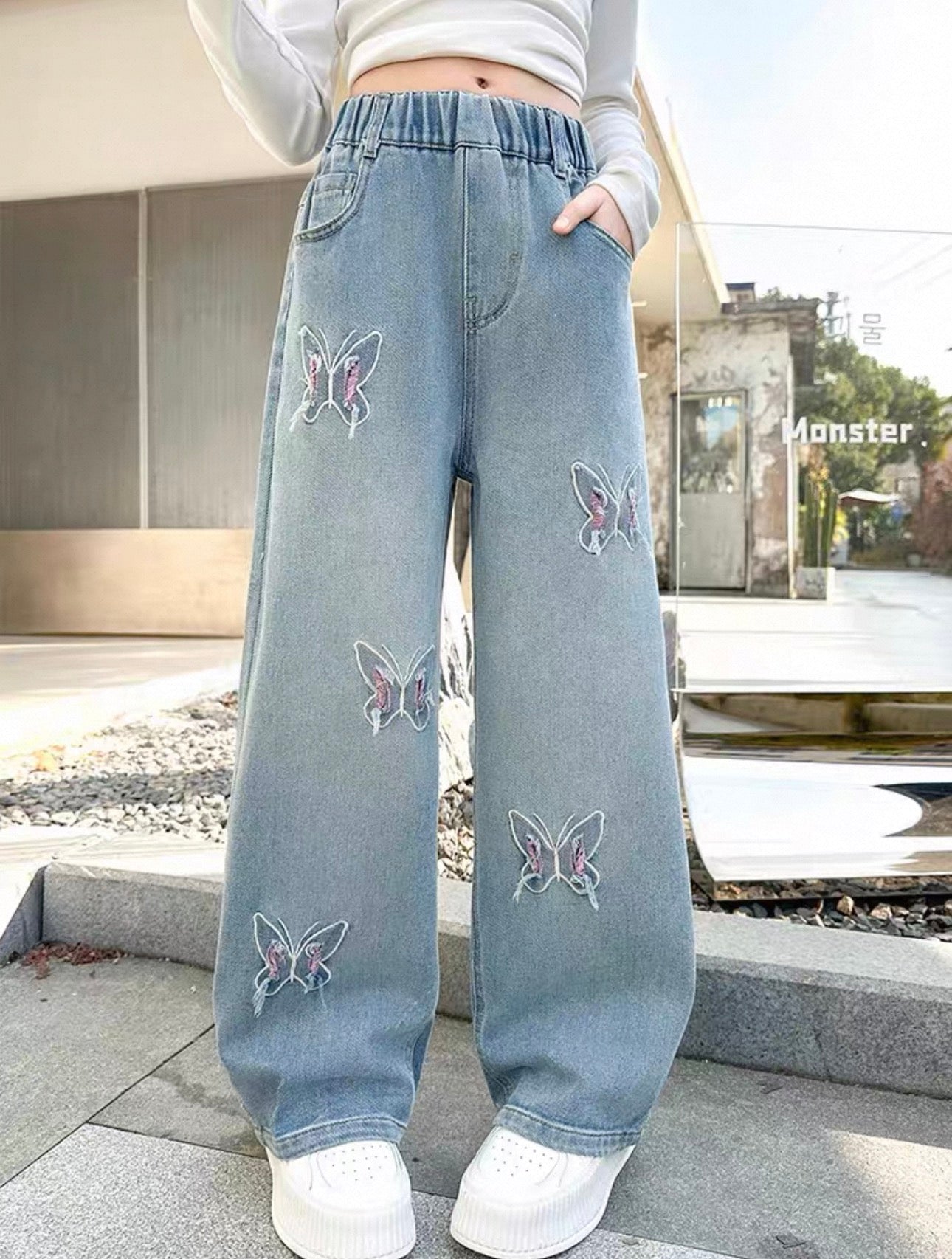 Light blue jeans with butterfly embroidery worn by a person outdoors.