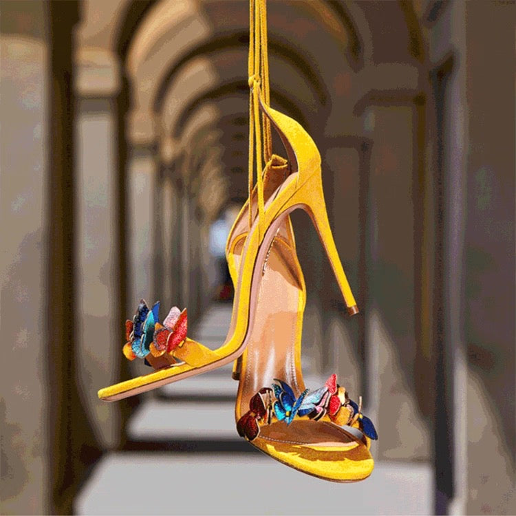 Yellow stiletto high heel sandals with one strap and multicolored butterfly decorations on the toe strap.