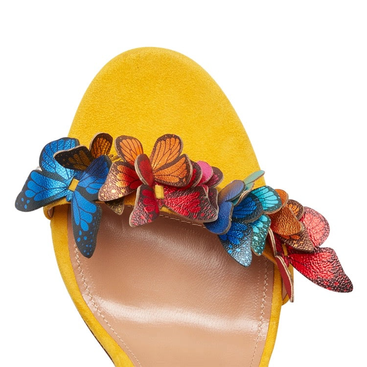 Yellow sandal with colorful butterfly and flower embellishments on one strap.