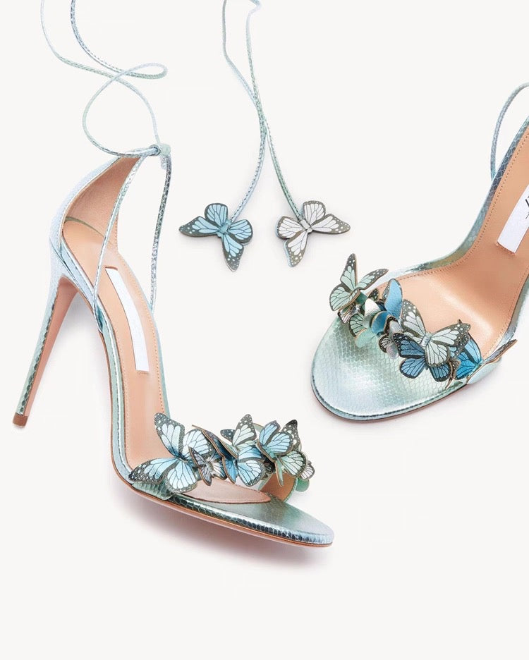 Light blue stiletto high heels with butterfly and flower embellishments and ankle wrap straps.