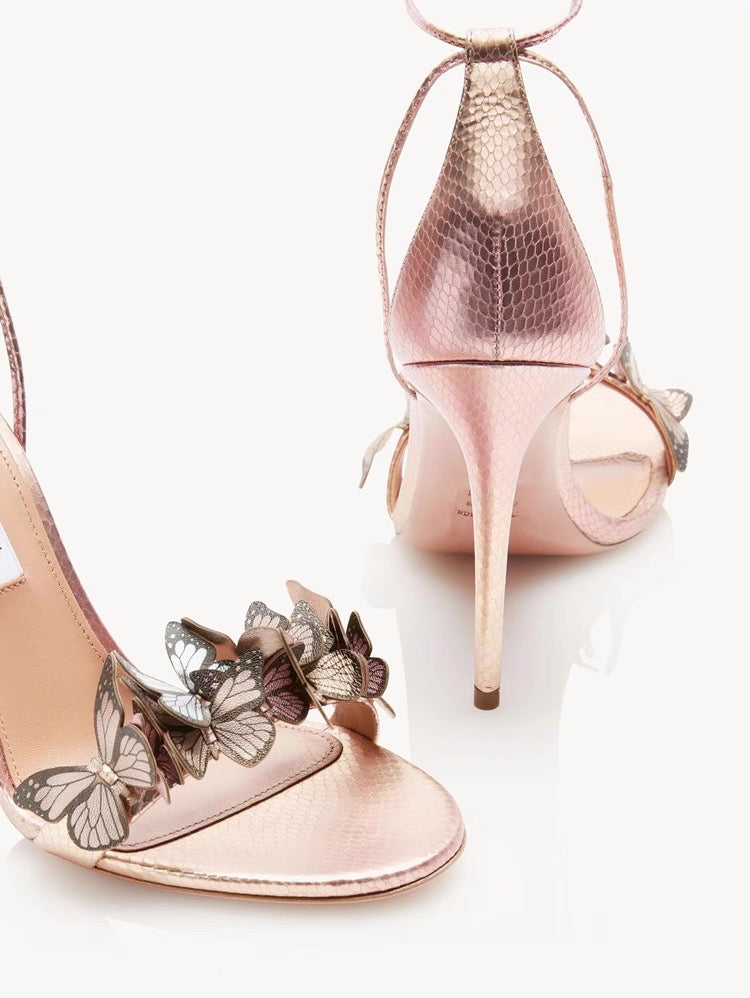 Pink satin stiletto heels with butterfly and flower embellishments, ankle wrap straps.