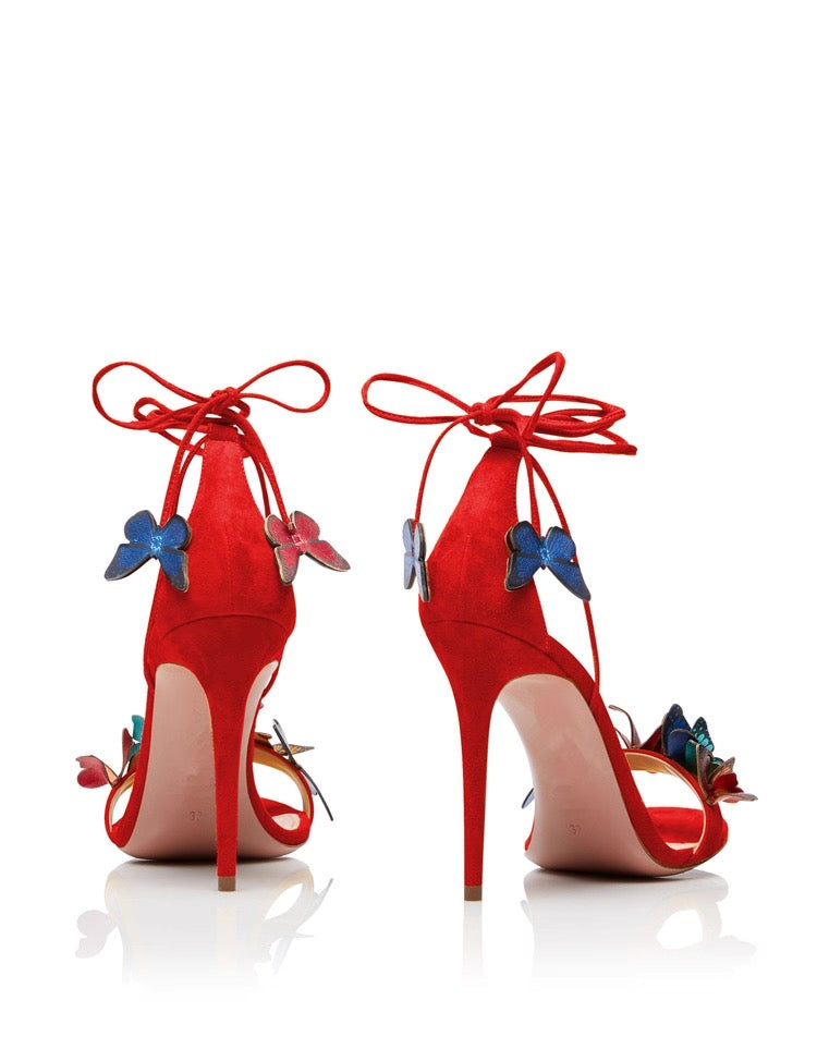 Red stiletto high heels with ankle wraps and colorful butterfly decorations on straps.