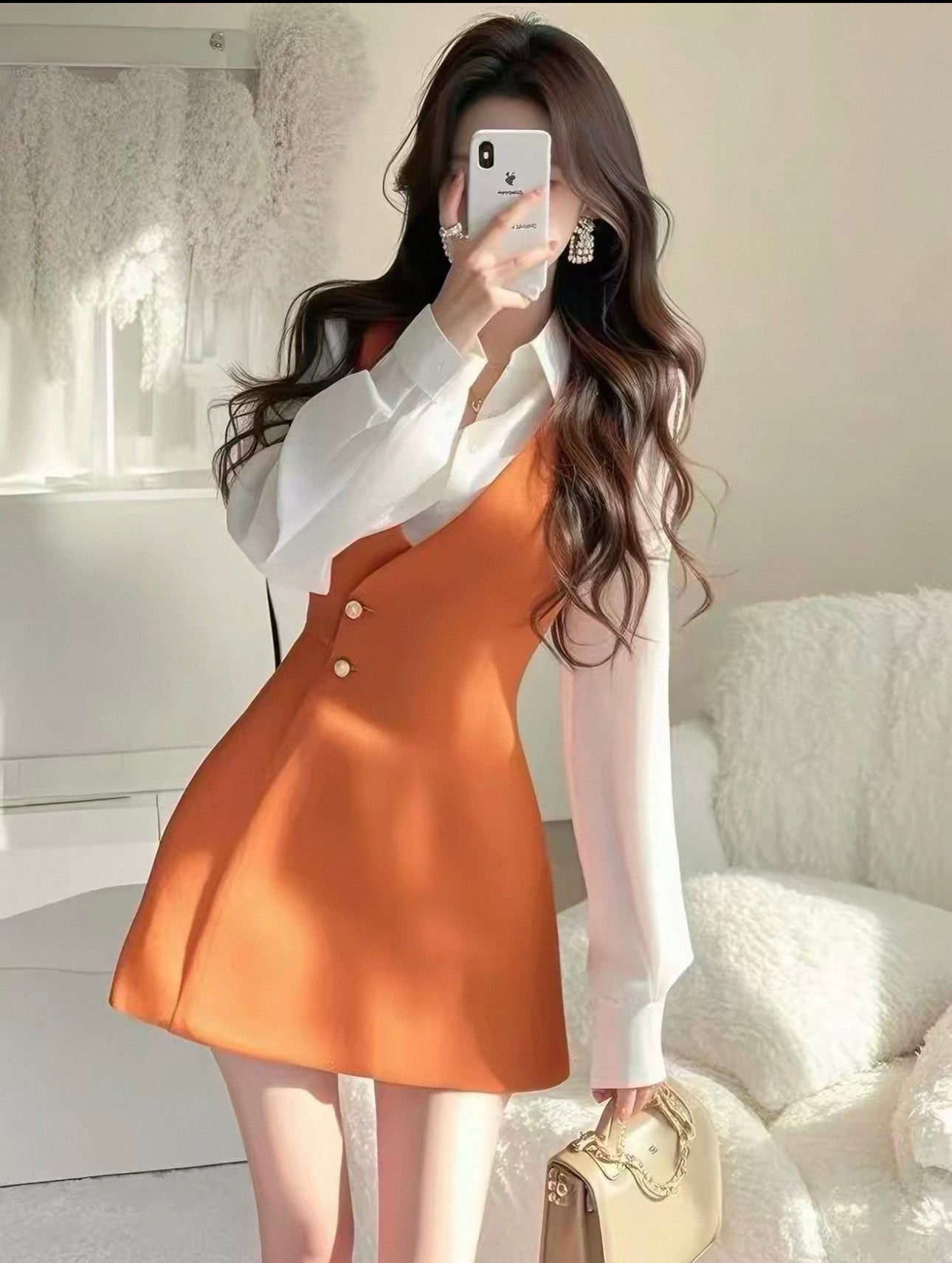 Woman taking a mirror selfie wearing a white shirt and orange dress.