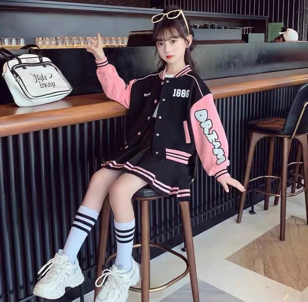 Person wearing a black and pink varsity jacket sitting on a bar stool in a casual setting.