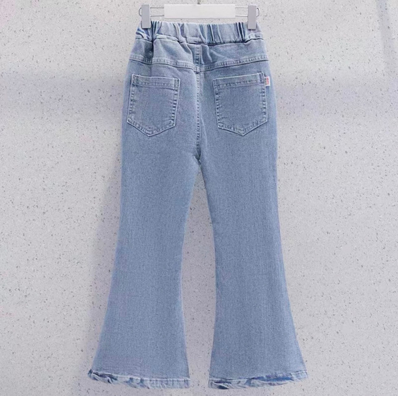Light blue flared jeans on a white hanger against a light gray background