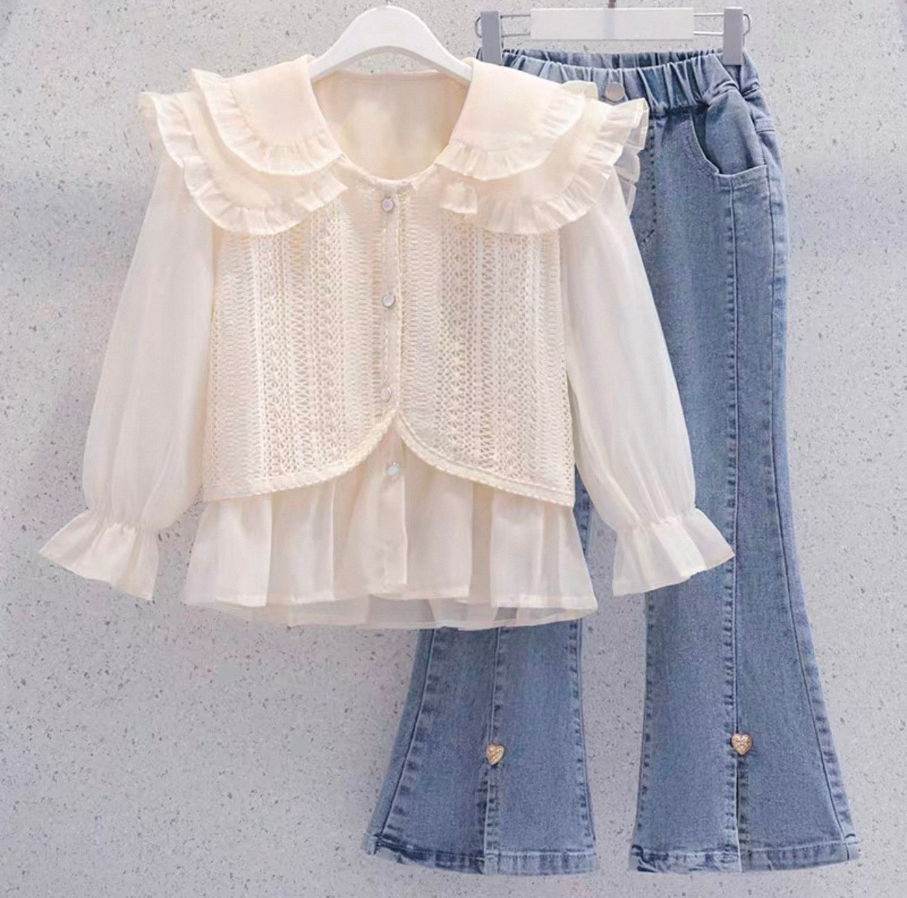 White lace blouse and blue jeans on hangers against a light gray background