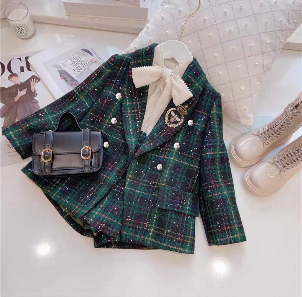 Green plaid blazer with decorative bow, black handbag, and beige boots on a white surface.