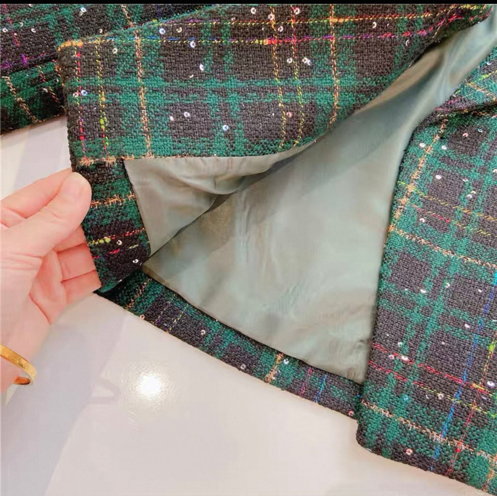Close-up of a green plaid fabric with sequins held by a hand.