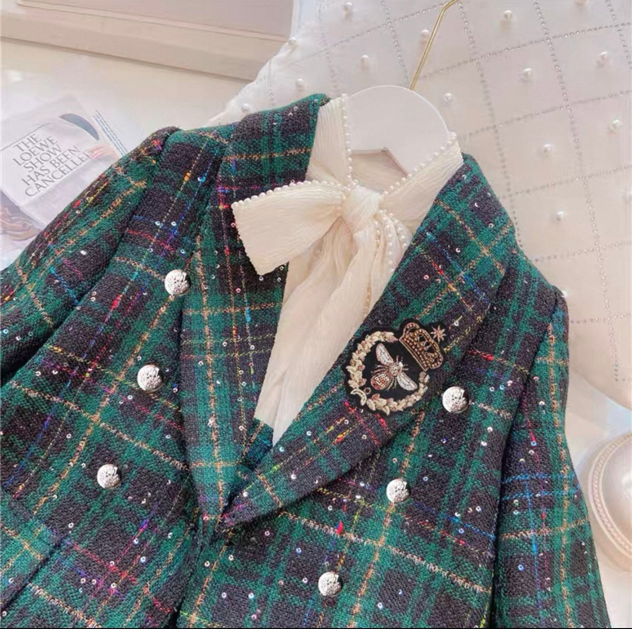 Green plaid blazer with decorative buttons and a white bow on a hanger.