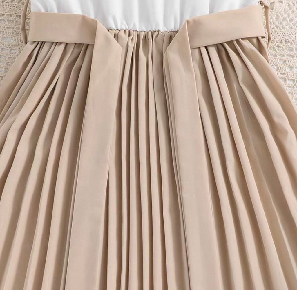 Close-up of a beige pleated skirt with a white top underneath.