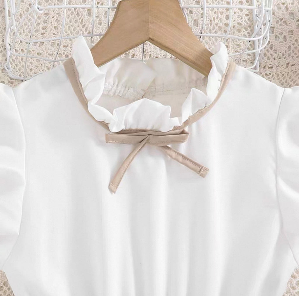 White blouse with ruffled collar and bow tie on a wooden hanger against a lace curtain background