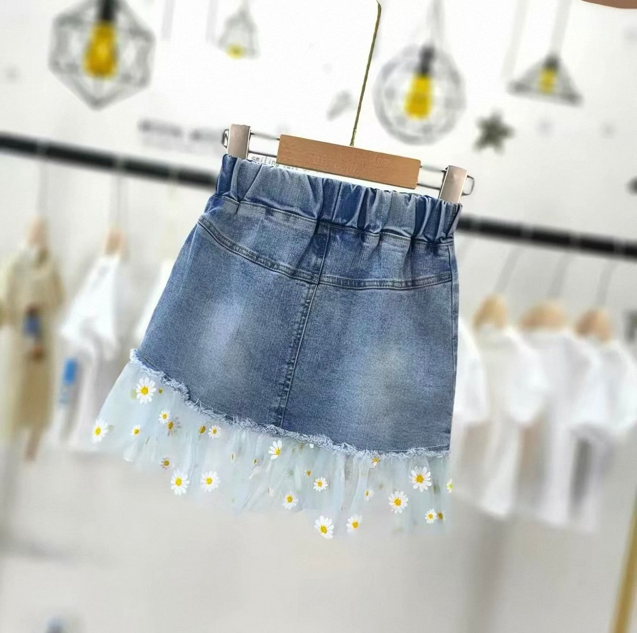 Denim skirt with floral hem on a hanger against a blurred background
