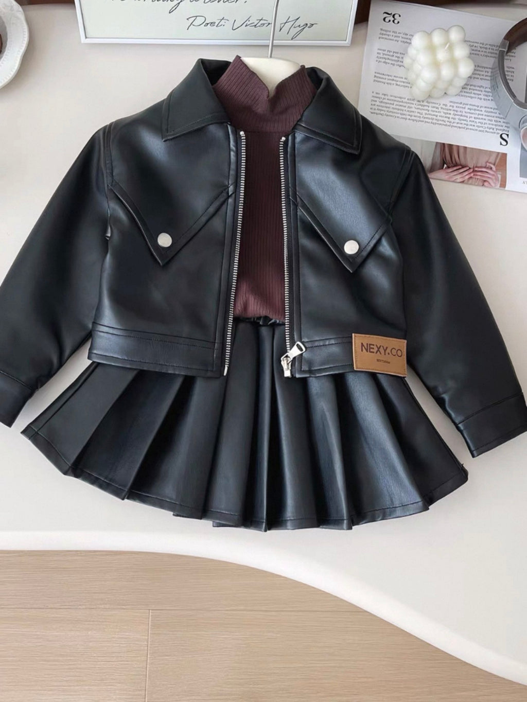 Black leather jacket and skirt set on a white surface with a magazine in the background.