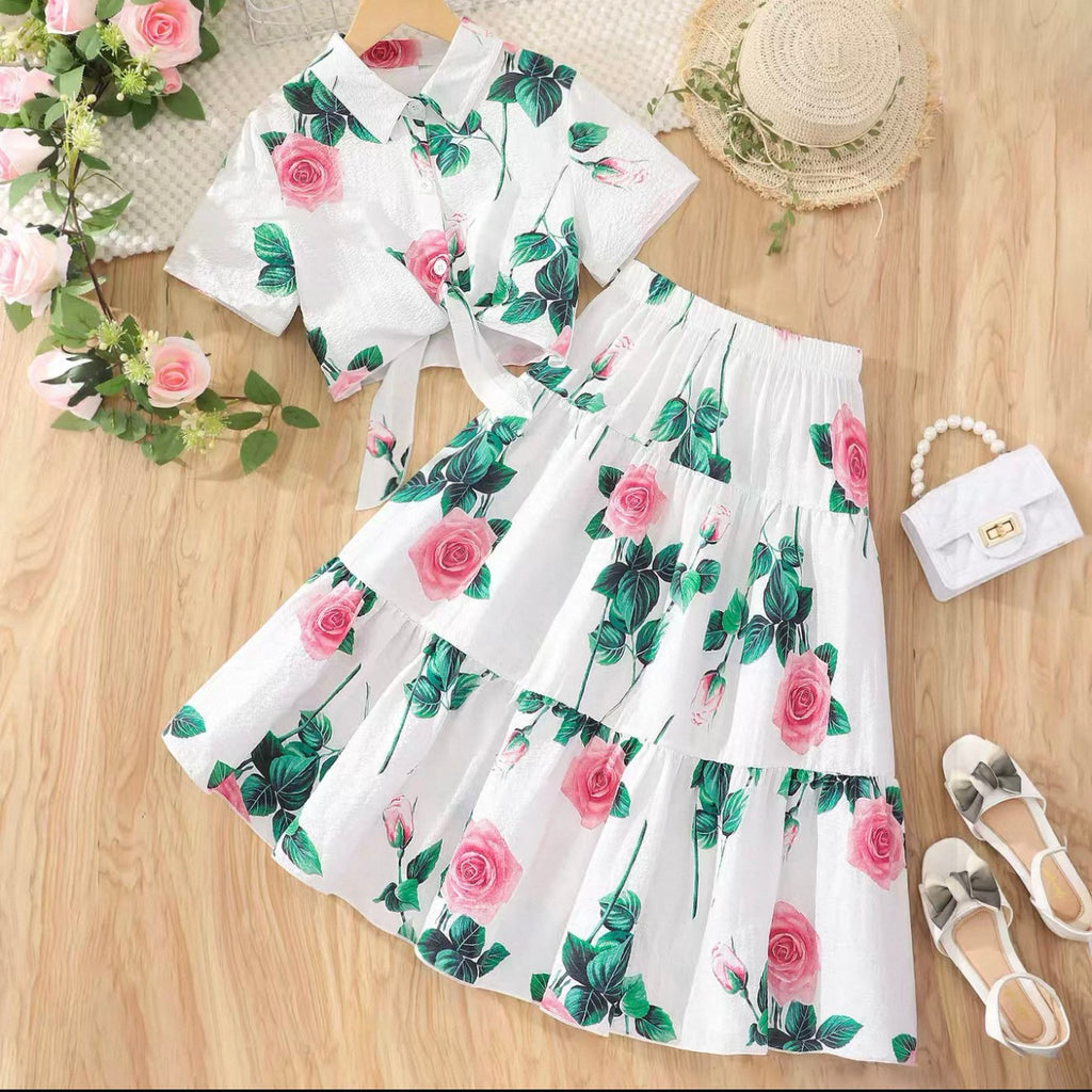 Floral outfit with top and skirt on a wooden surface, accompanied by shoes and a handbag.