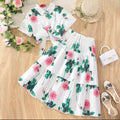 Floral outfit with top and skirt on a wooden surface, accompanied by shoes and a handbag.