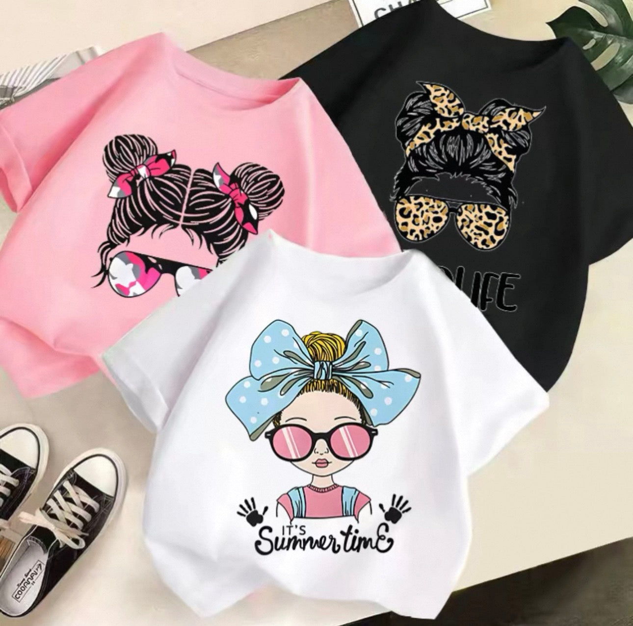 Three t-shirts with graphic designs of hairstyles and a shoe on a light background