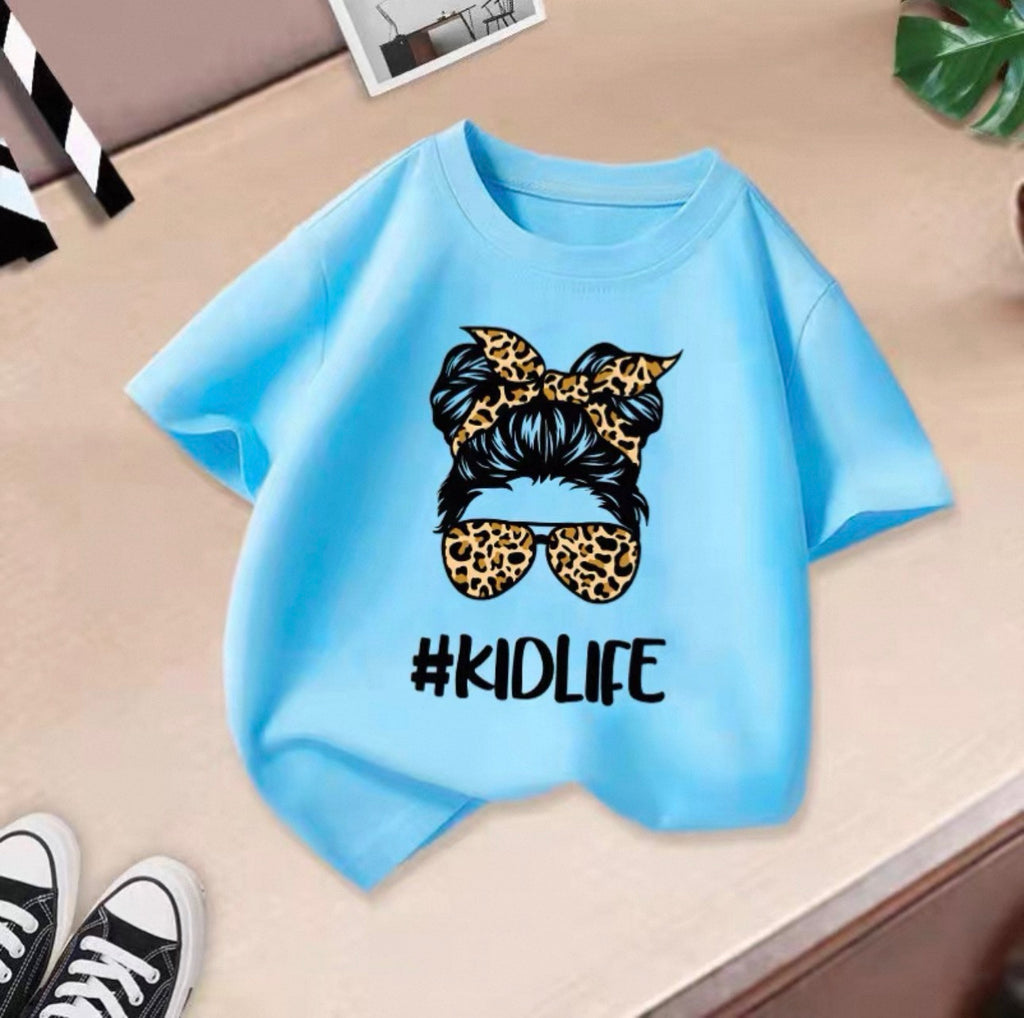 Light blue t-shirt with '#KIDLIFE' design featuring a leopard print headband and sunglasses on a beige surface.