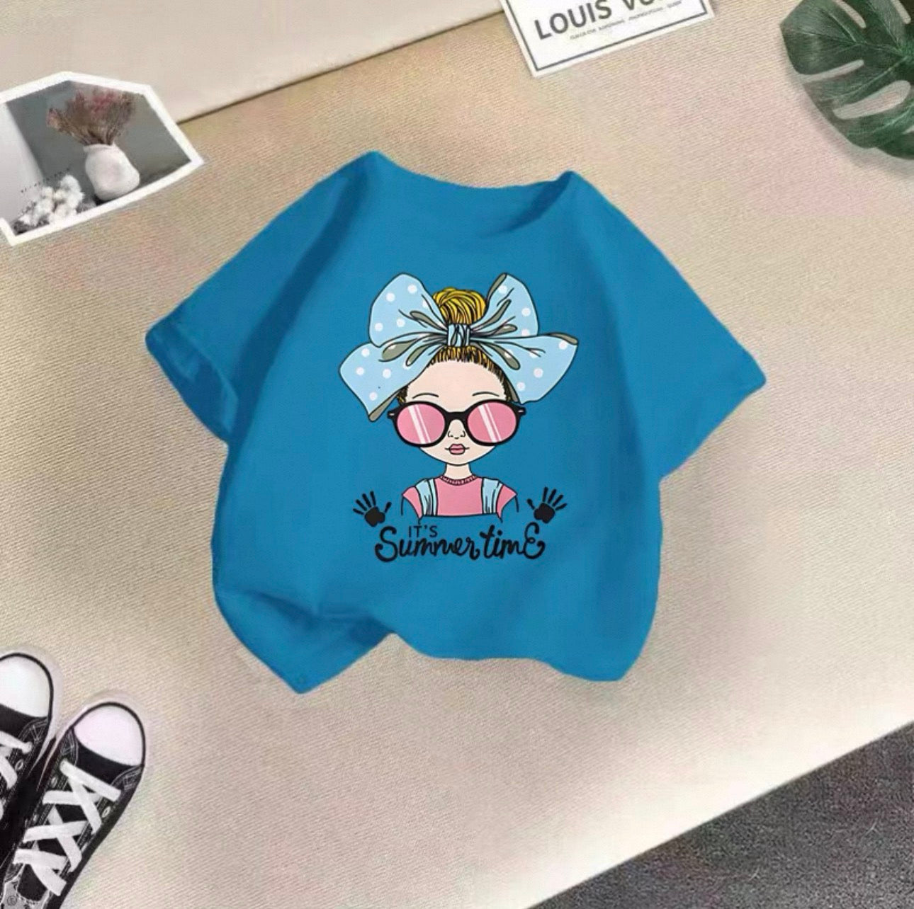 Blue sweatshirt with a cartoon design and 'It's Summertime' text on a beige surface.