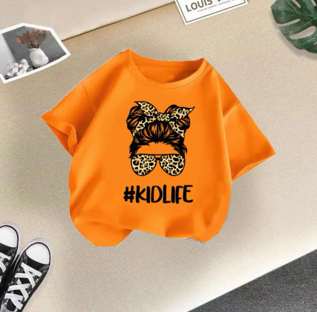 Orange t-shirt with '#KIDLIFE' design on a beige surface