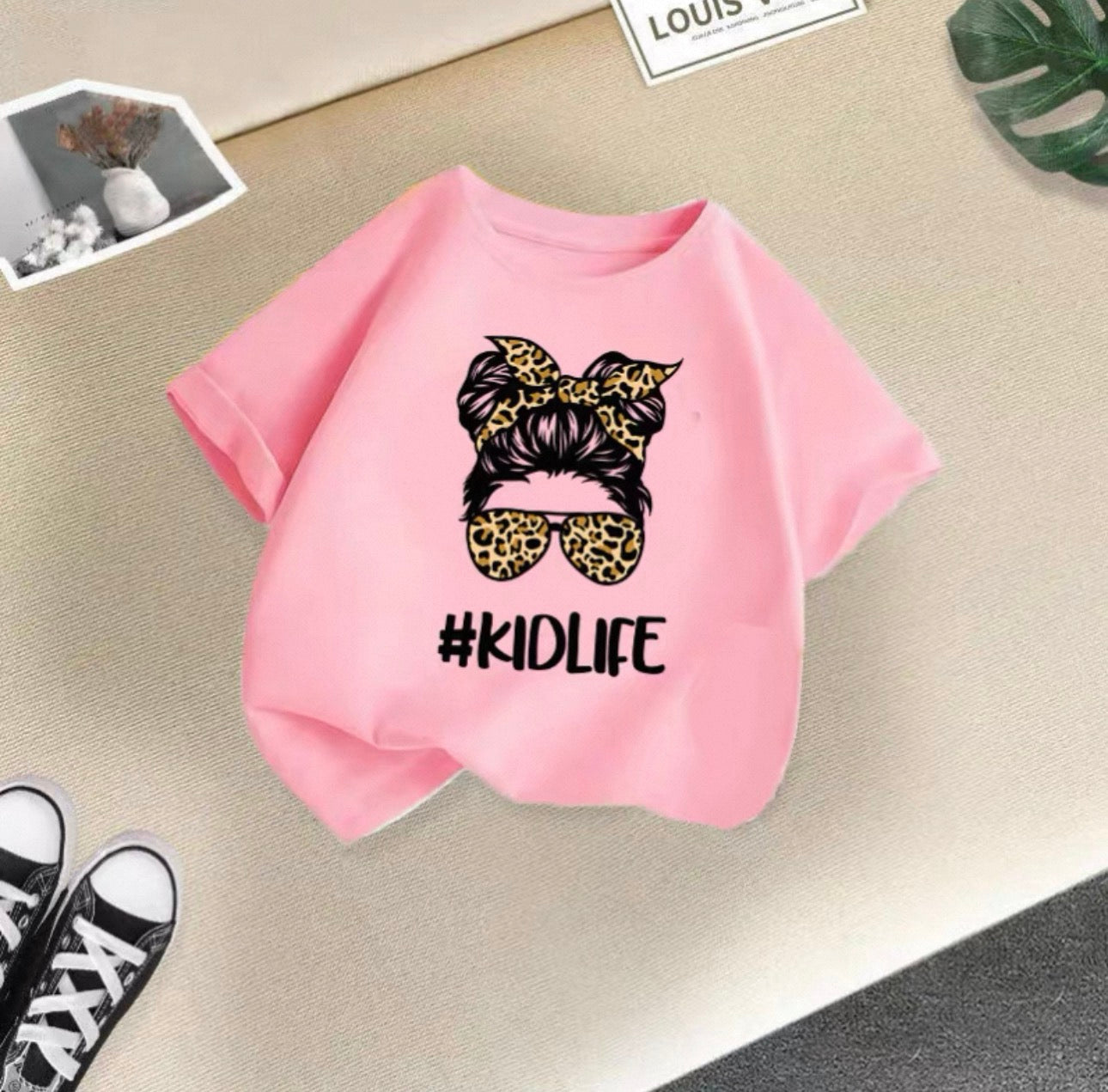 Pink t-shirt with graphic design and '#KIDLIFE' text on a light surface.