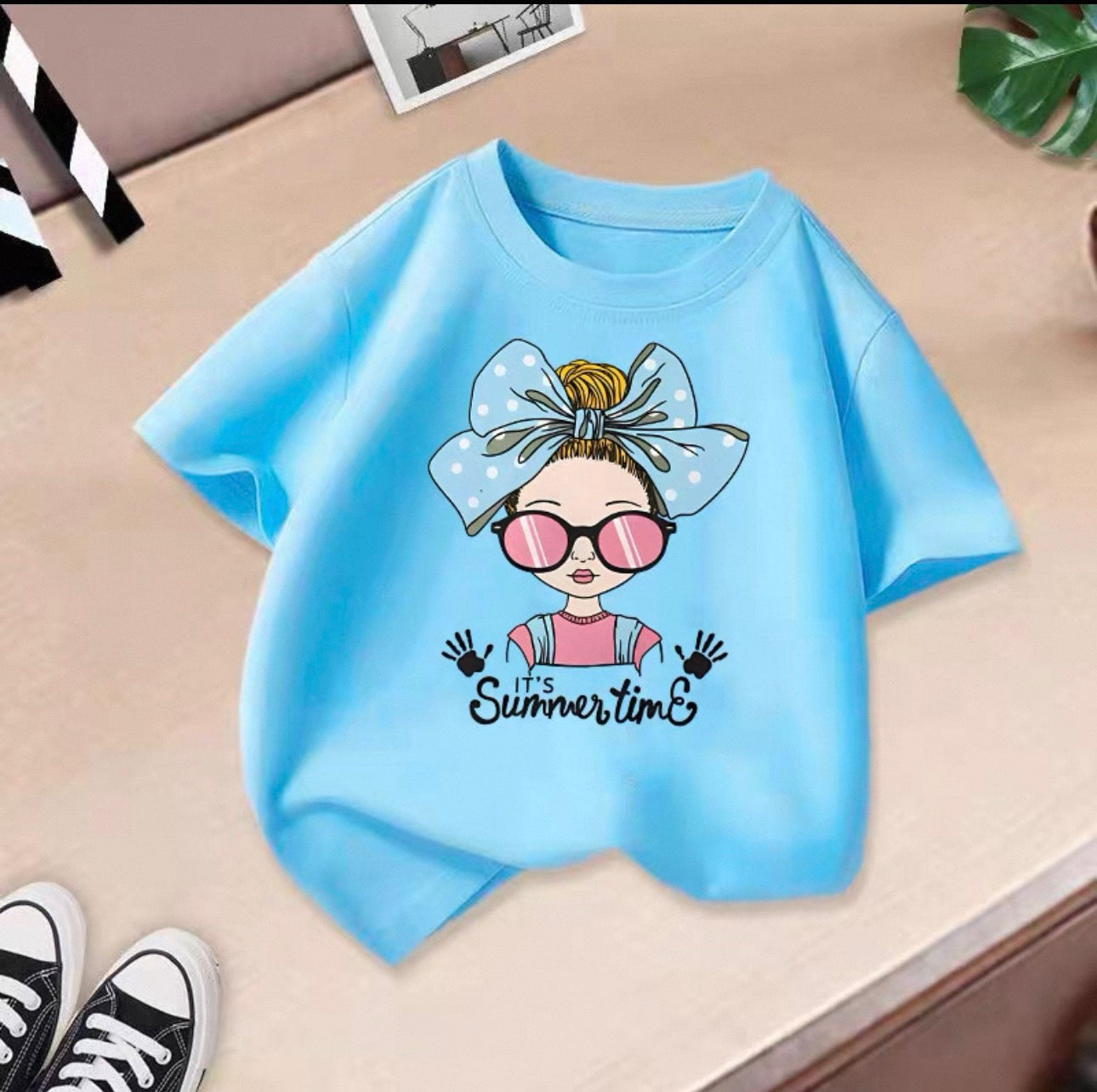 Blue t-shirt with a cartoon character and 'It's Summertime' text on a beige surface.