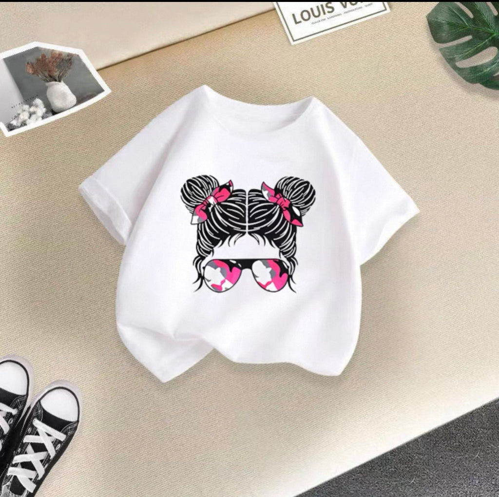 White t-shirt with a graphic design of hair buns and sunglasses on a beige surface.