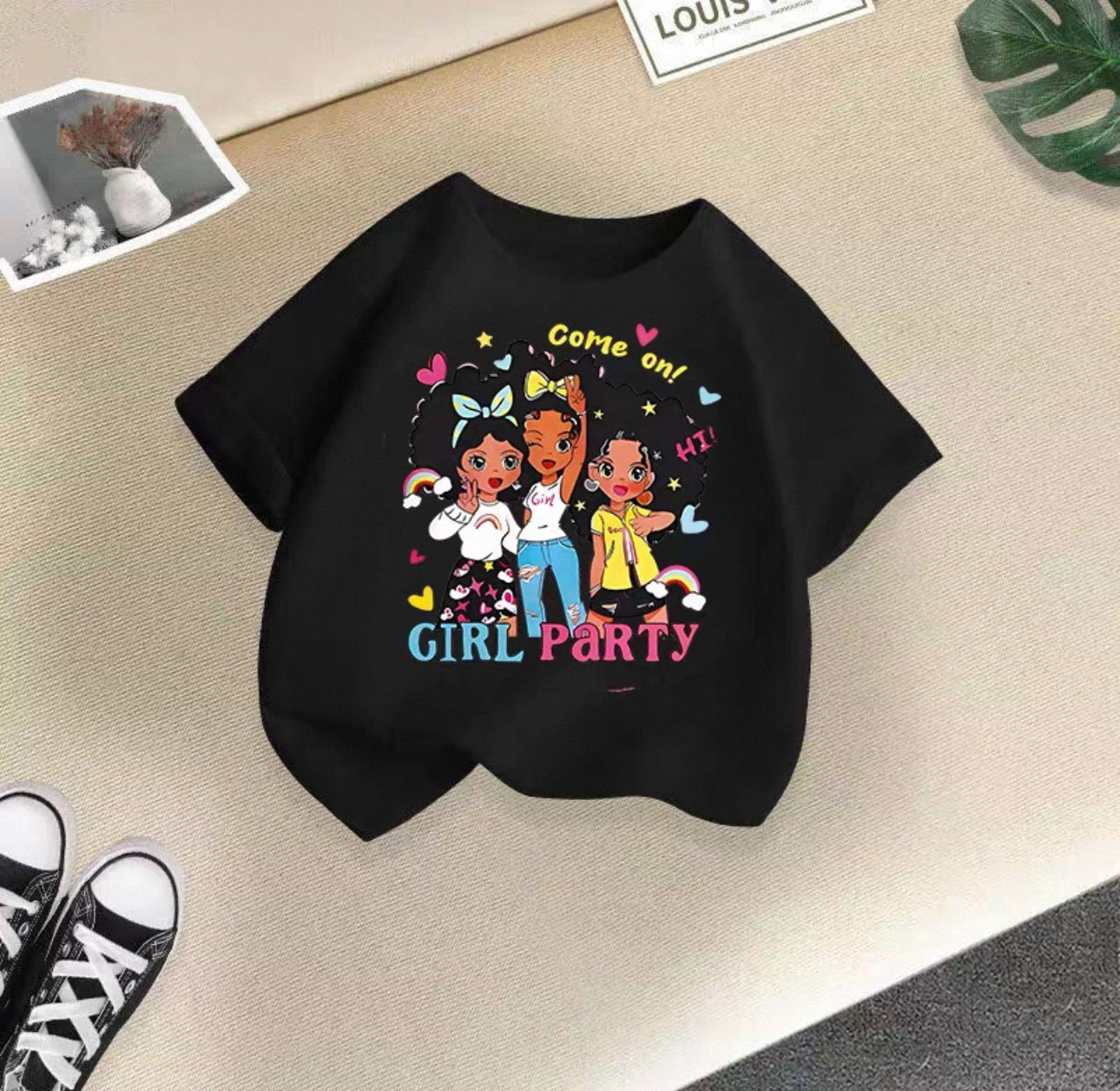 Black t-shirt with colorful graphic design of three girls and text on a beige surface.