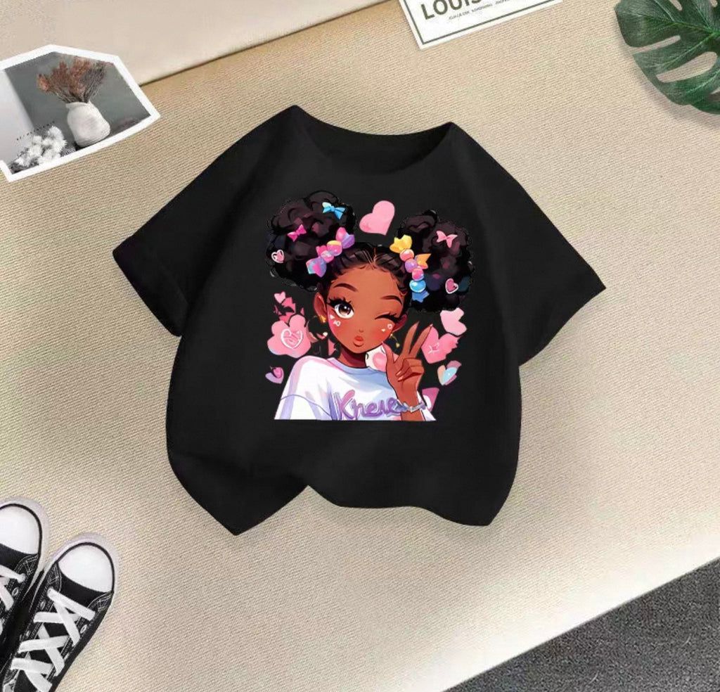 Black t-shirt with a colorful graphic of a girl with braids and flowers on a beige surface.