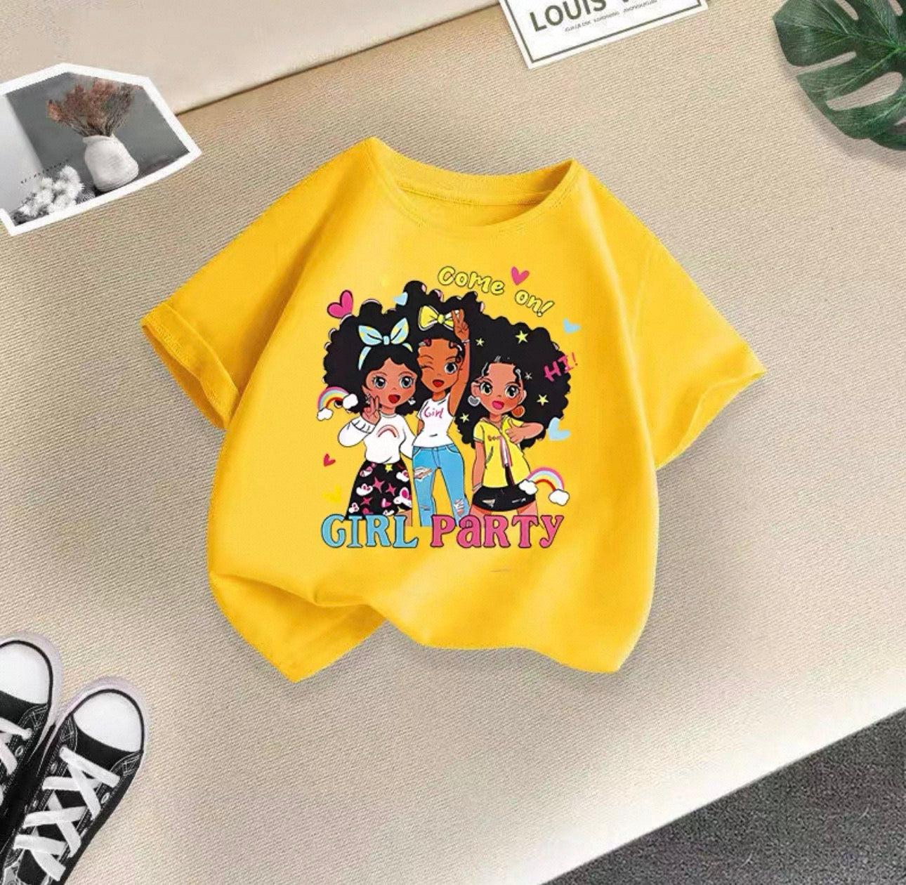 Yellow t-shirt with cartoon girls and 'Girl Party' text on a beige surface.
