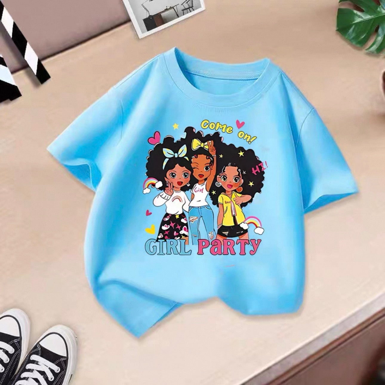 Light blue t-shirt with cartoon girls and text on a beige surface