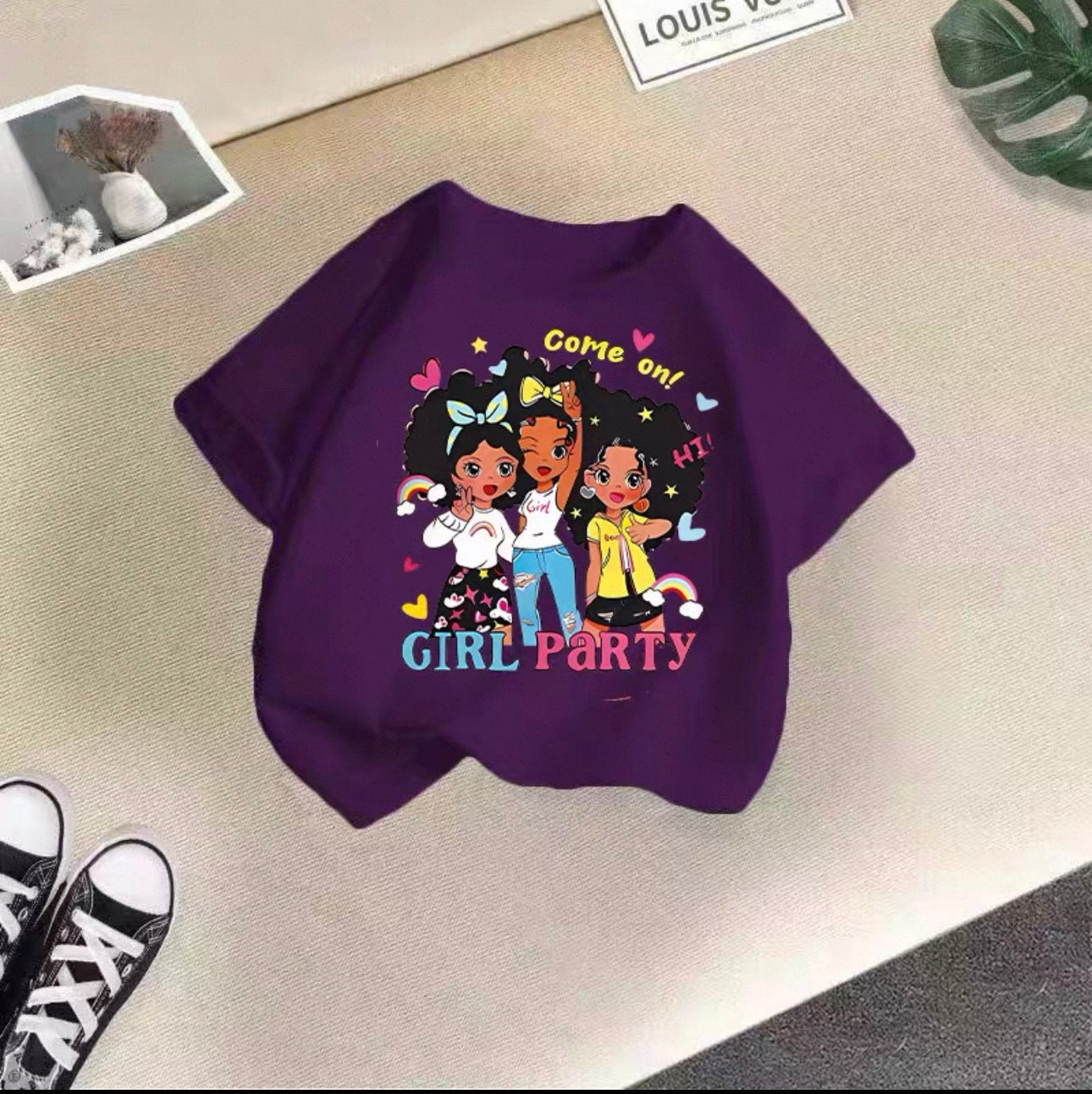Purple shirt with cartoon girls and 'Girl Party' text on a beige surface
