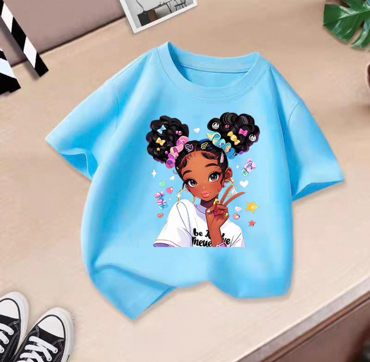 Light blue t-shirt with an illustration of a girl with styled hair on a beige surface.