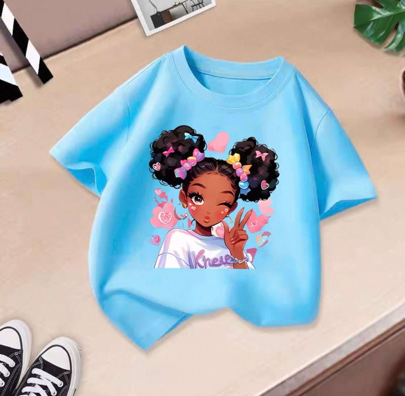 Blue t-shirt with an illustration of a girl with styled hair on a beige surface.