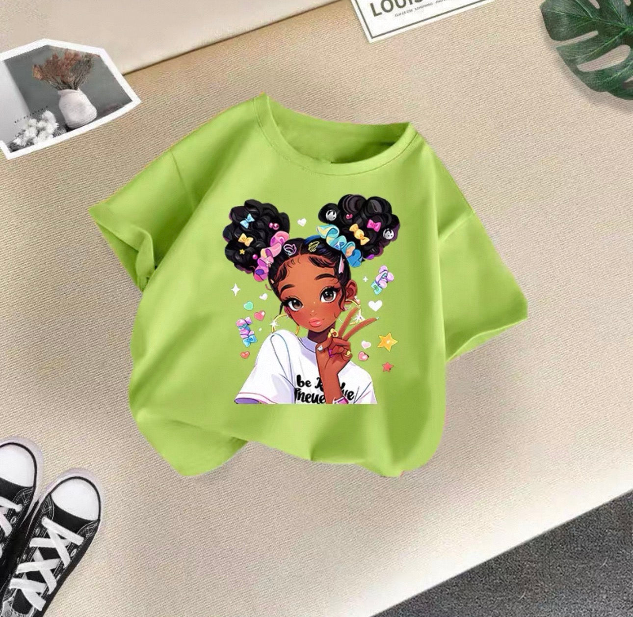 Green sweatshirt with a graphic of a girl with braids and colorful accessories on a beige surface.
