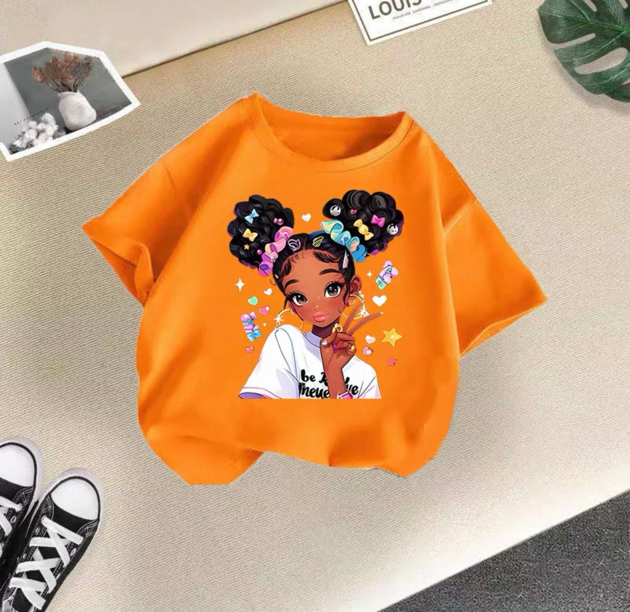 Orange sweatshirt with a graphic of a girl with braids on a beige surface.
