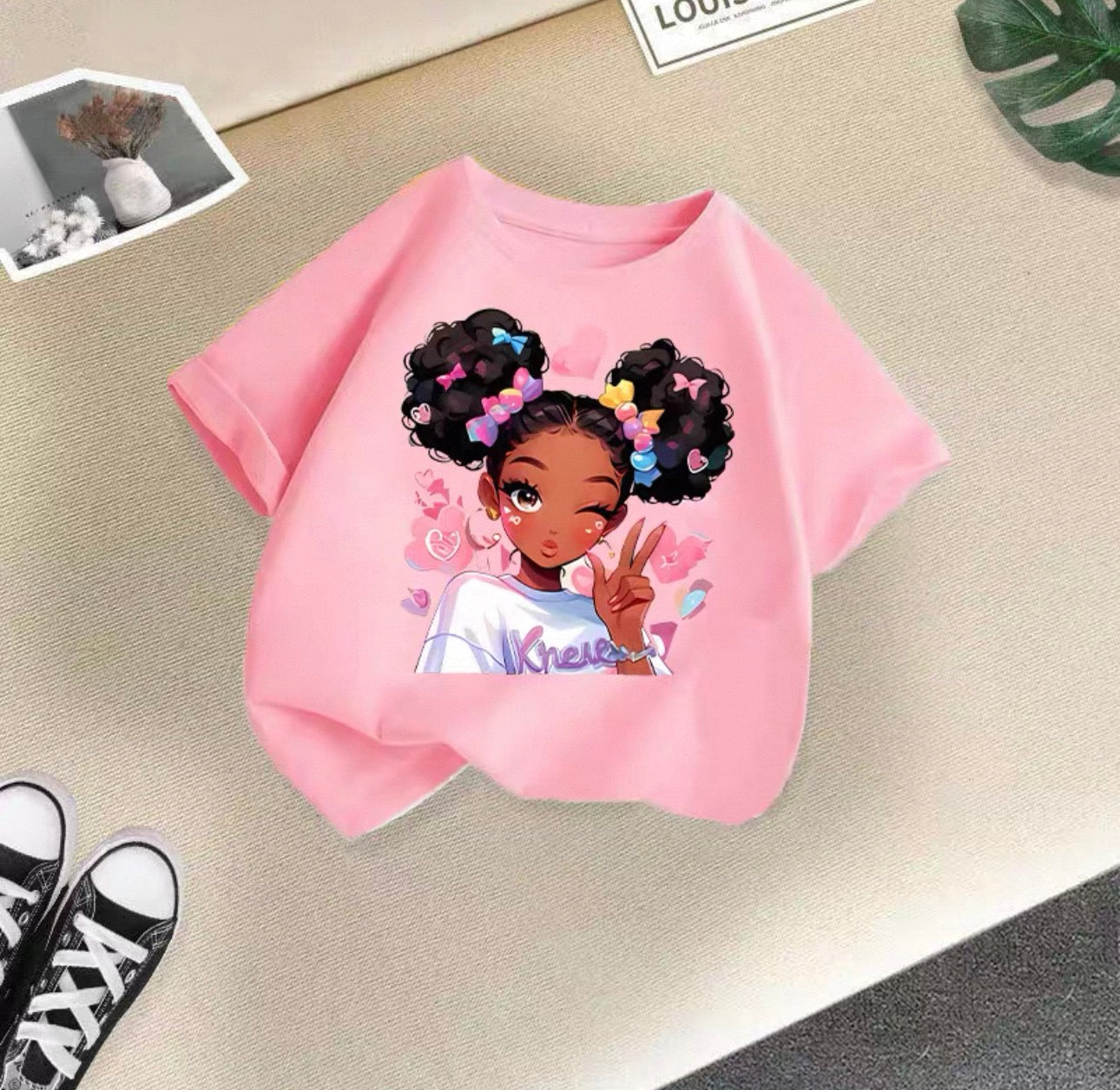 Pink t-shirt with a graphic of a girl with colorful hair on a beige surface.