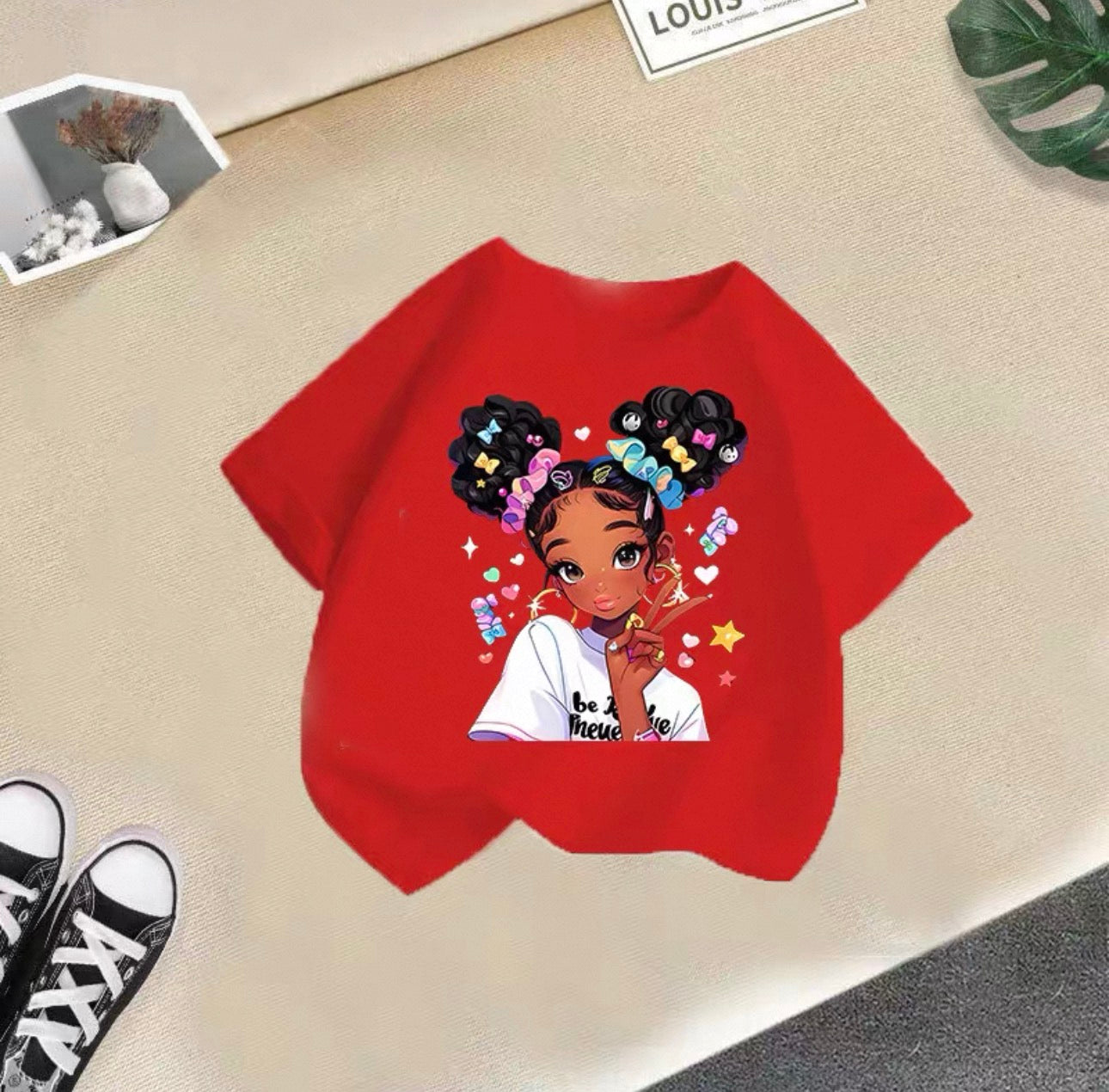 Red t-shirt with a graphic of a girl with styled hair on a beige surface.