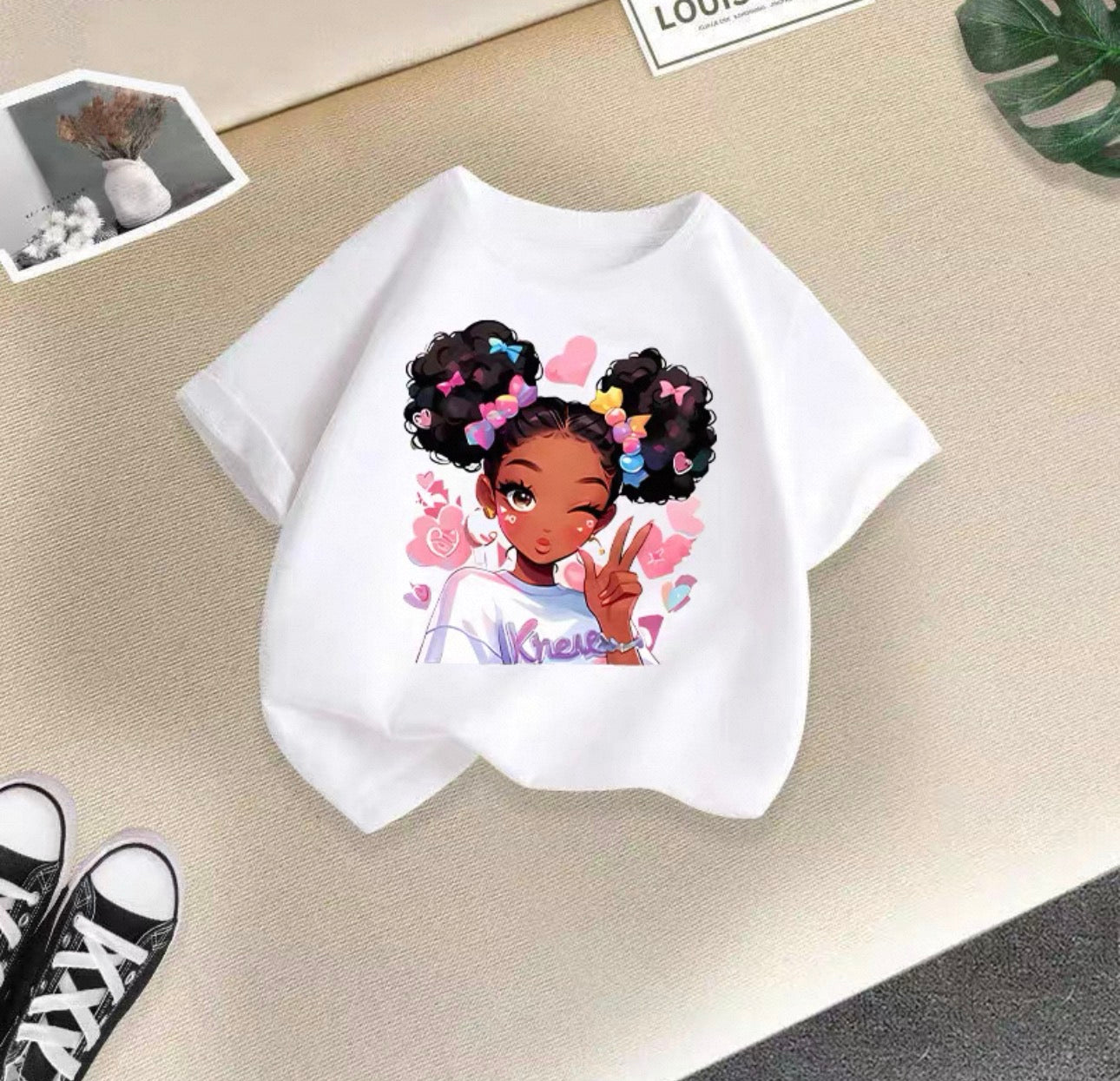 White t-shirt with a colorful graphic of a girl on a beige surface.