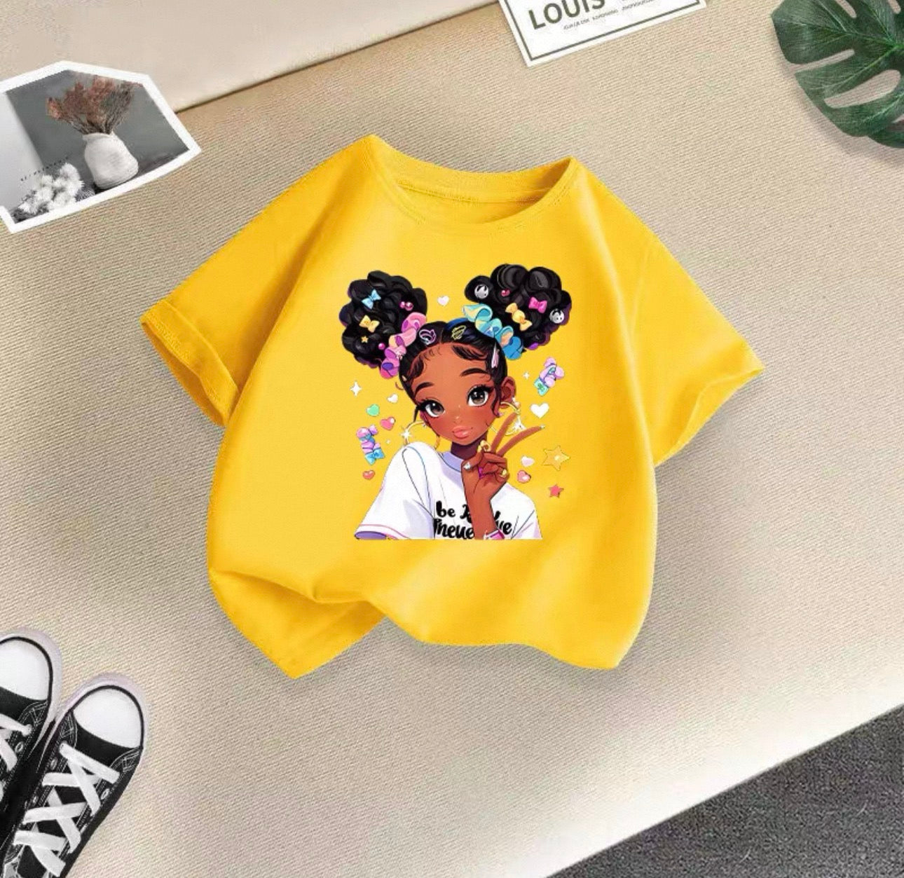 Yellow t-shirt with a graphic of a girl with styled hair on a beige surface.
